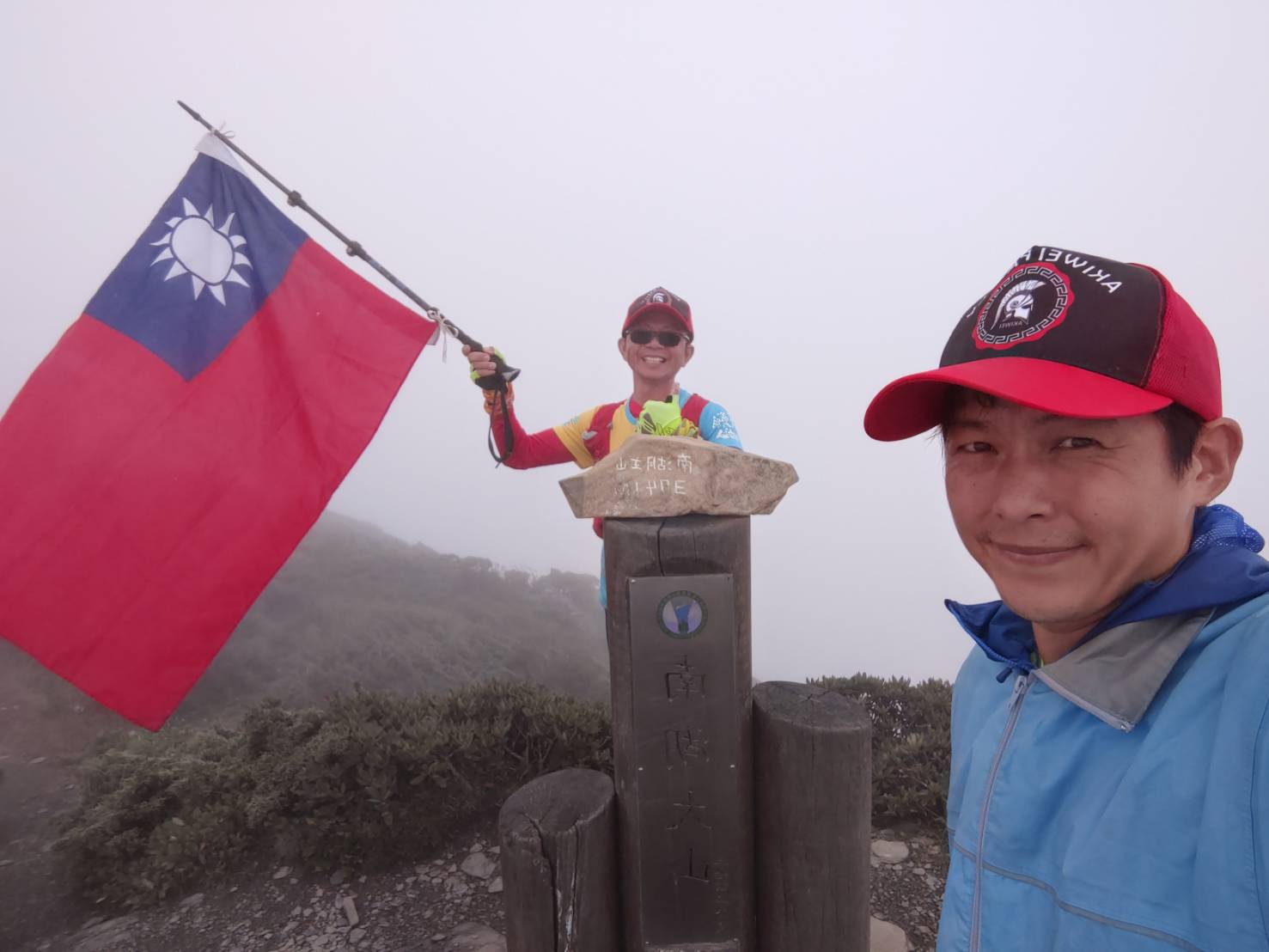 林慶華與林俊良開心舉起國旗與南湖大山碑石合影